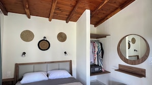 Un dormitorio con techo de madera, una cama con colcha gris, un espejo redondo y un perchero.