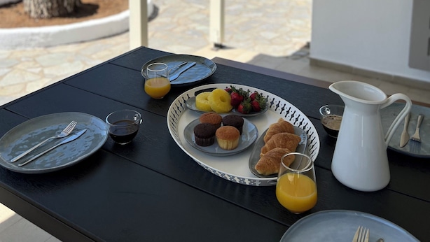 Un espacio de comedor al aire libre con una mesa preparada para el desayuno, incluyendo platos, cubiertos y una jarra.