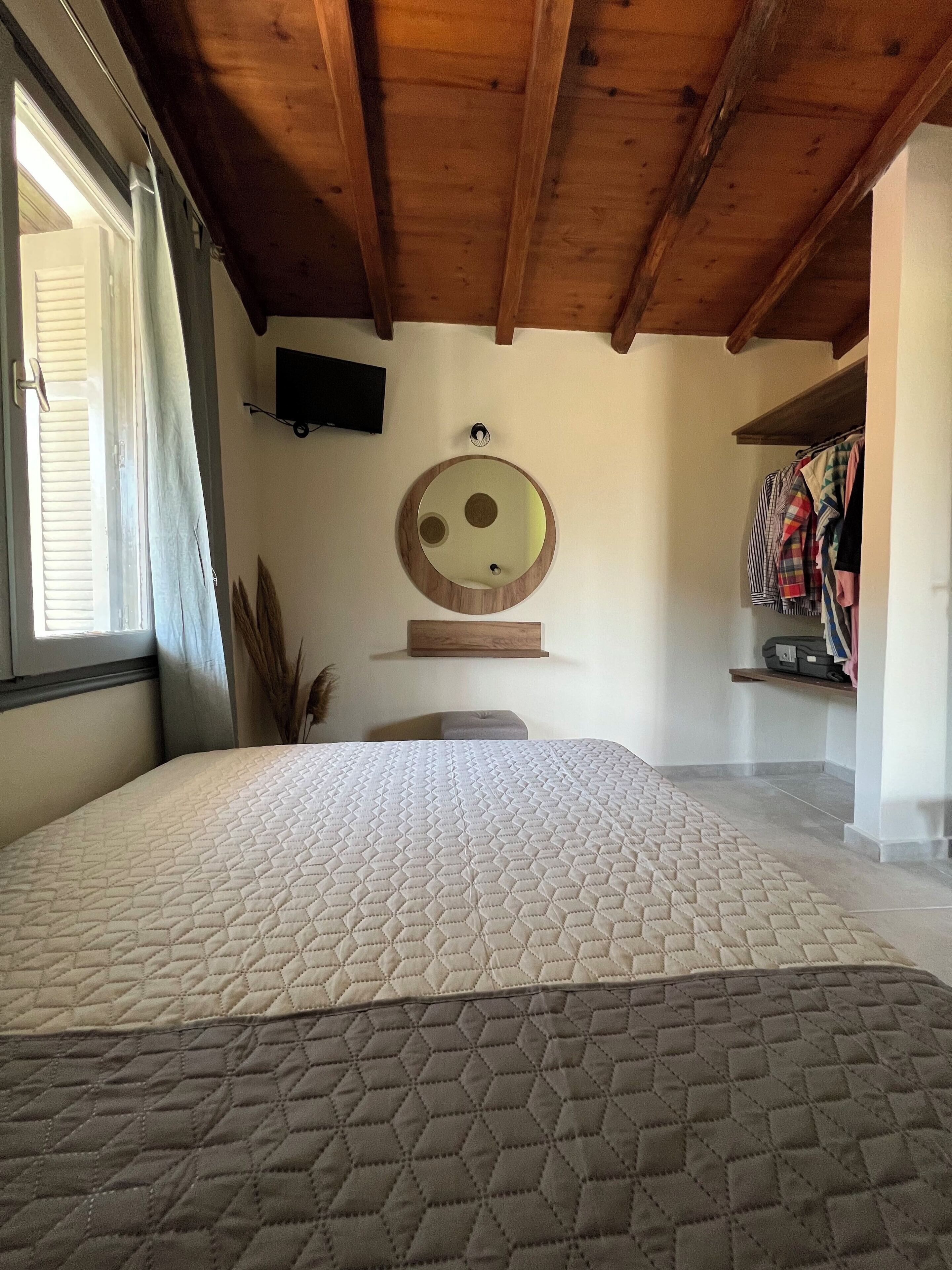 A bedroom with a bed, a round mirror, a television, and a wardrobe.