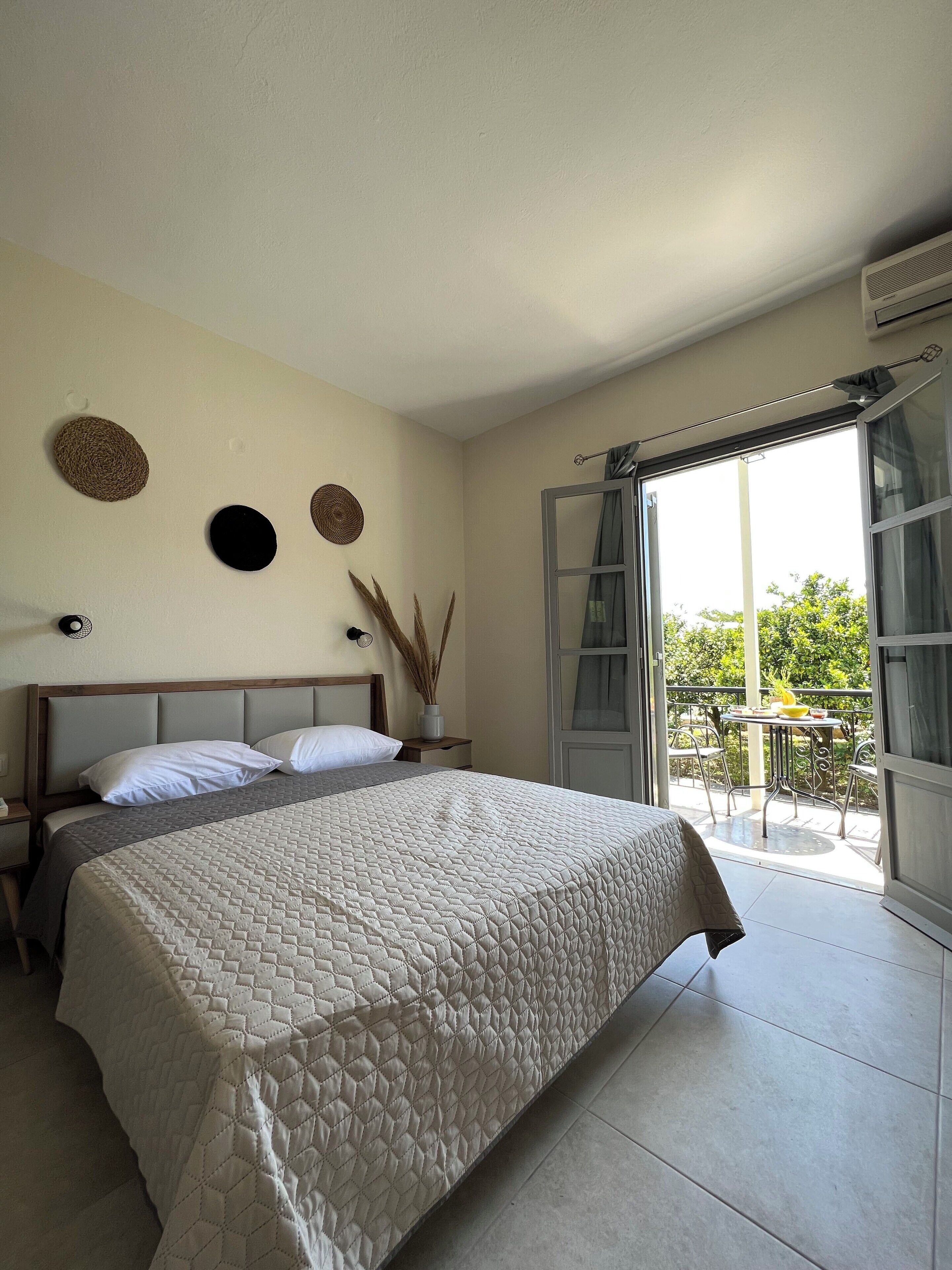 Una camera da letto con un letto, un comodino, una sveglia a parete e vista su un balcone esterno.