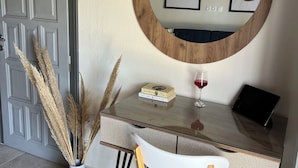 Una habitación con escritorio, silla, espejo redondo, planta en maceta y copa de vino.