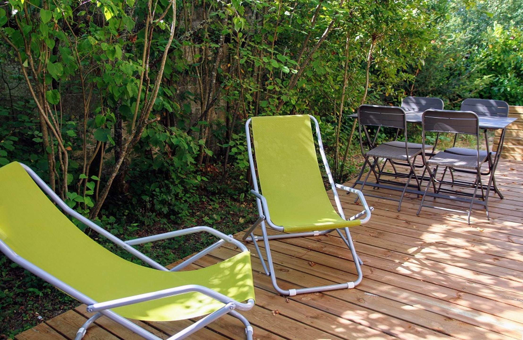 A wooden deck with two green lawn chairs and a table with chairs.