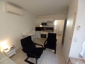 Espaço compacto com cozinha compacta, duas cadeiras pretas, uma mesa de cabeceira pequena e uma luminária.