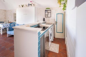 A compact kitchen with a washing machine, a sink, and a dining area with a table and chairs. - Mono Judeca by BarbarHouse (Vieste)