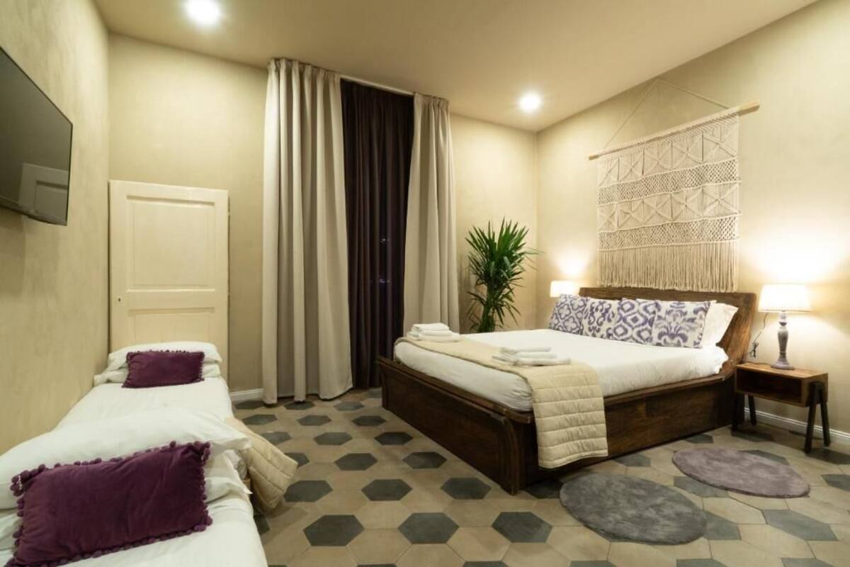 A bedroom with a bed, two bedside tables, a mirror, a plant, and a geometric-patterned wall hanging.