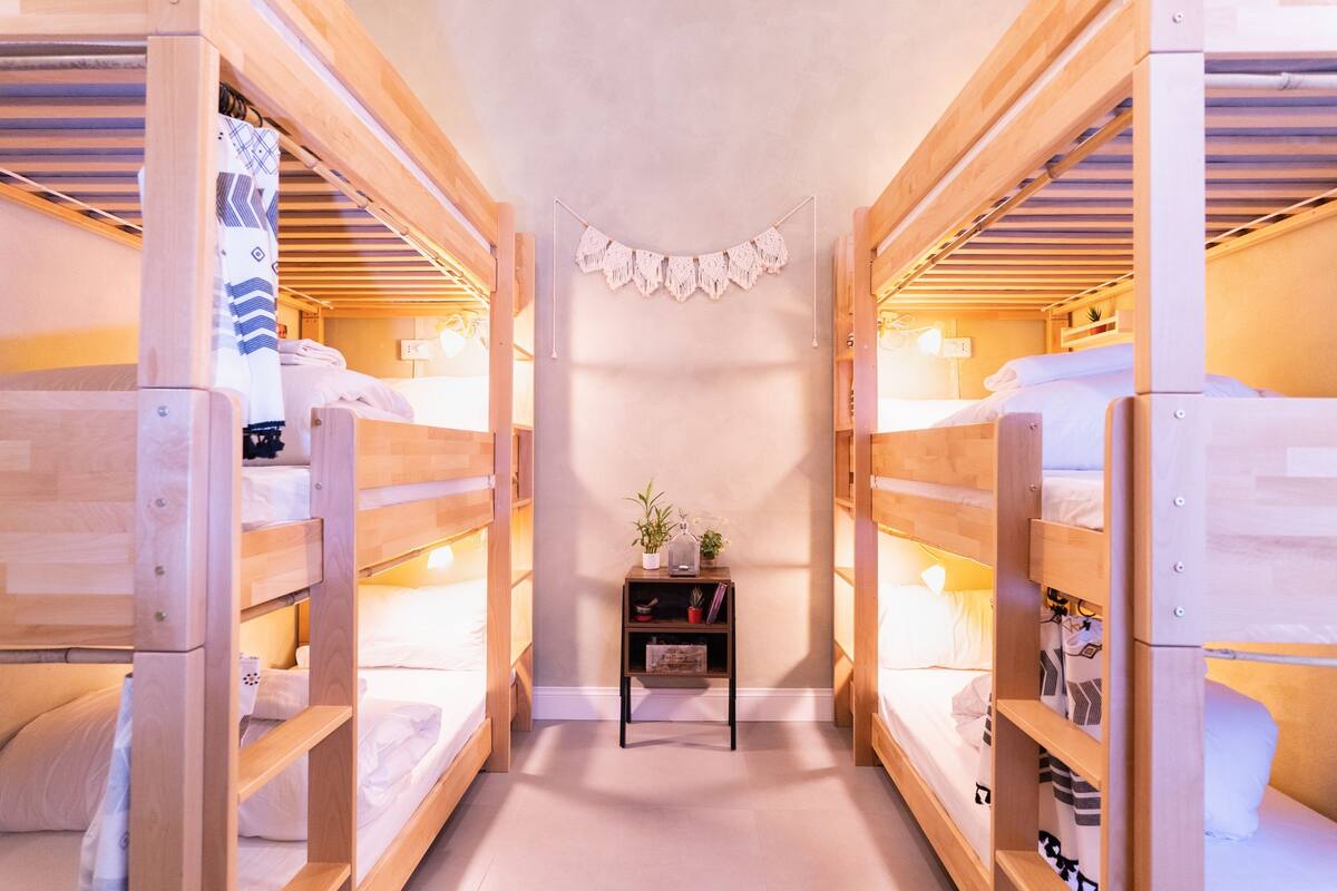 A room with bunk beds, a small table with a plant, and a macrame decoration.