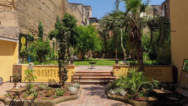 A courtyard with a palm tree, a fountain, and a garden area. - HOPESTEL Secret Garden Napoli (Naples)