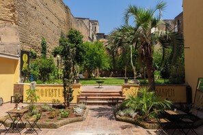 A courtyard with a palm tree, a fountain, and a garden area. - HOPESTEL Secret Garden Napoli (Naples)