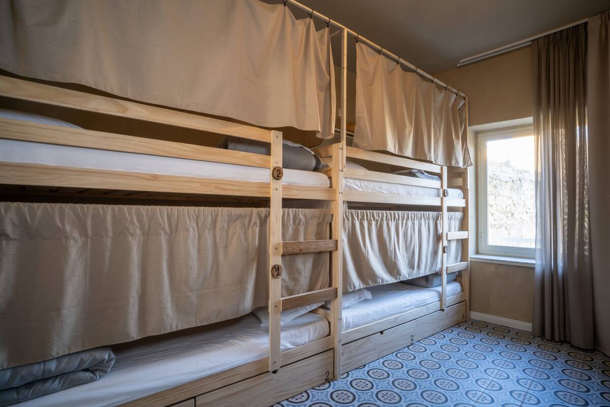 A bunk bed room with a window, curtains, and patterned floor.