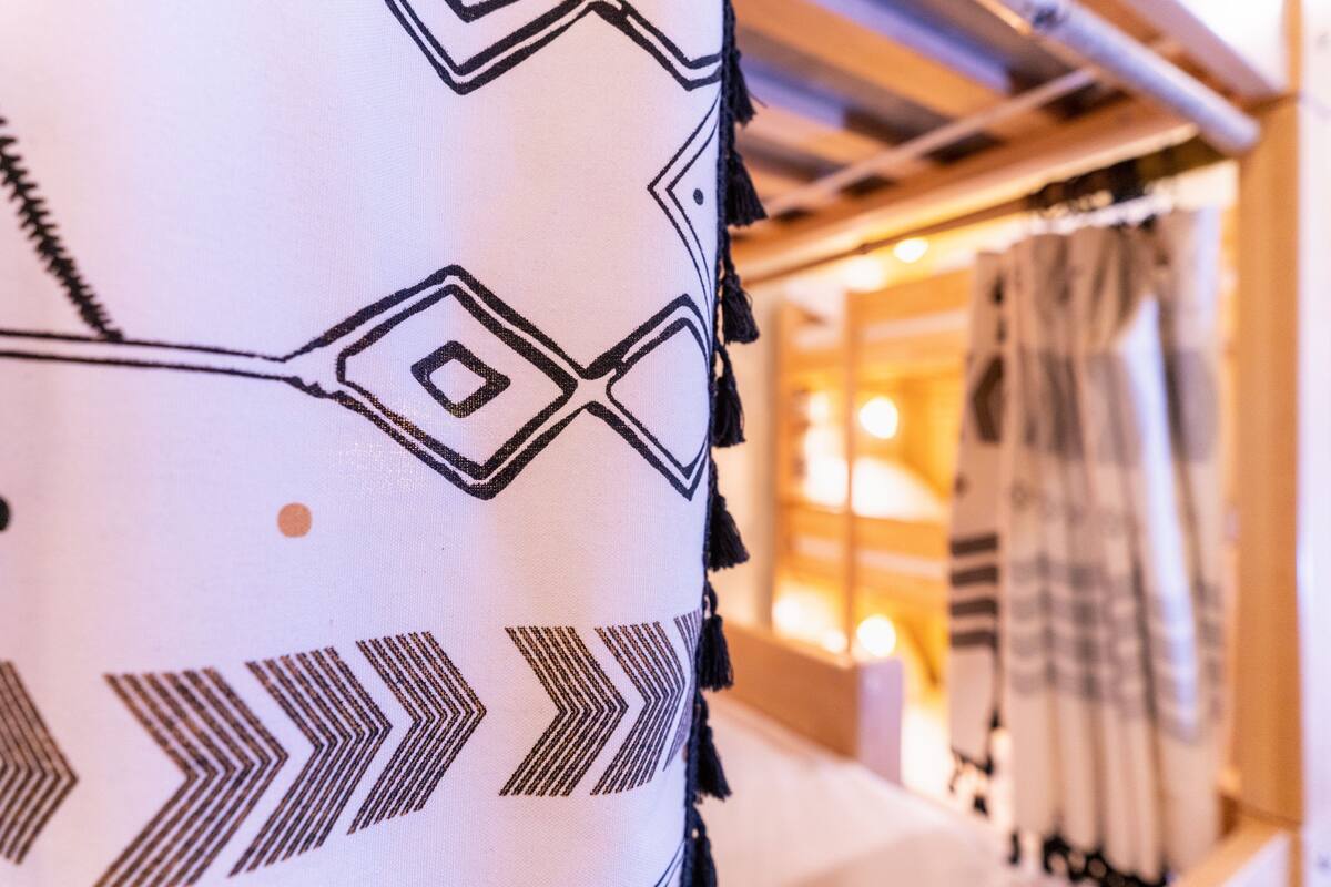 A close-up of a patterned pillow with geometric designs, a bed with a white headboard, and a room with a warm ambiance.
