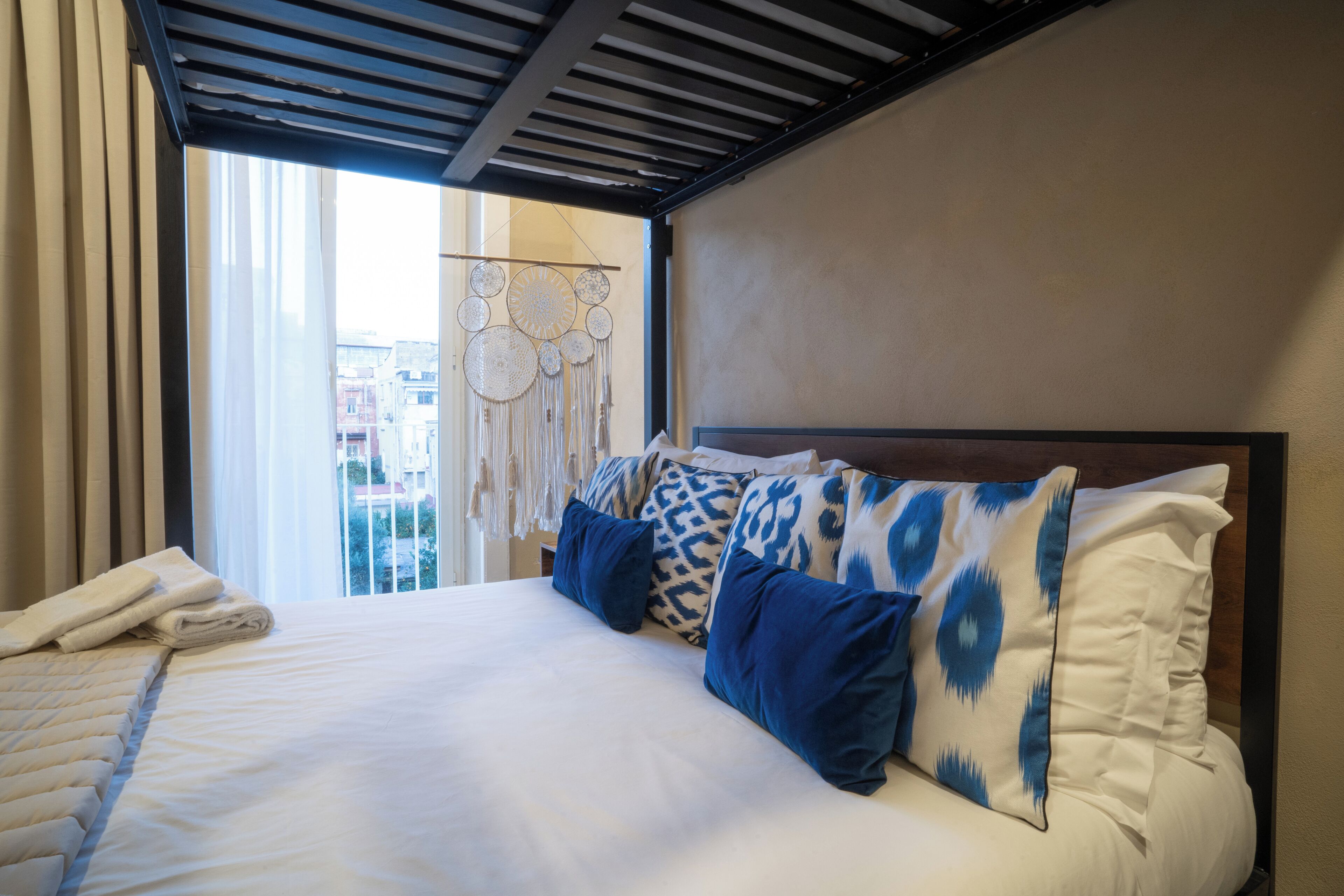 A hotel room with a bed, a view of the city, and a decorative wall hanging.