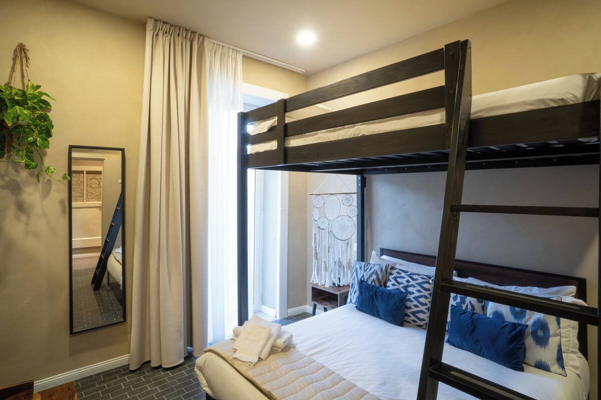 A bunk bed with a white mattress and blue pillows, a mirror on the wall, and a plant hanging above the bed.
