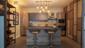 A modern kitchen with a central island, bar stools, hanging light fixtures, and wooden cabinetry. - HOPESTEL Secret Garden Napoli (Naples)