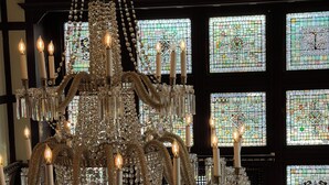A grand chandelier with multiple candle-like lights, surrounded by ornate crystal decorations.