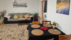 Una sala de estar con un sofá, una mesa de centro y una mesa de comedor con sillas. Hay un cuadro en la pared y una lámpara en el techo.