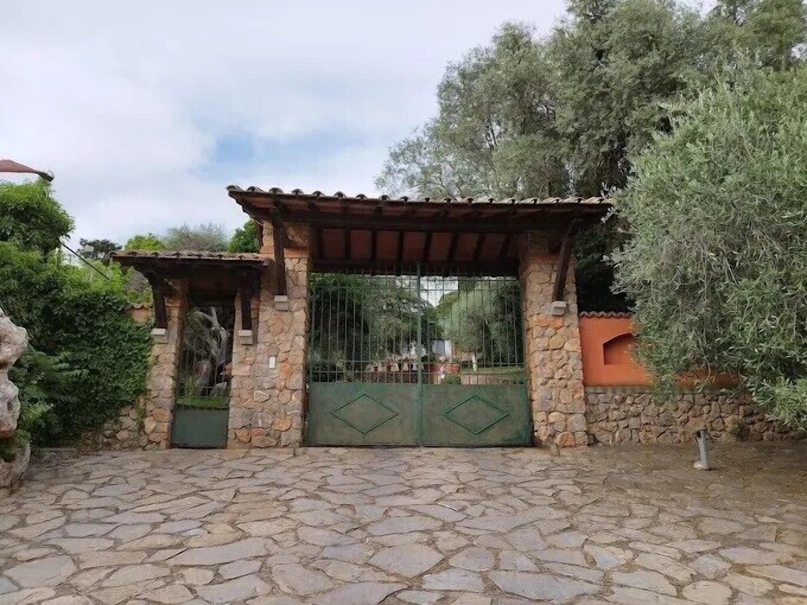 Un cancello in pietra con recinzione in metallo, un ingresso lastricato e una struttura a pergola.