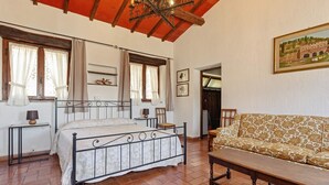 Een slaapkamer met een bed, een houten bankje, een sofa en een kroonluchter.