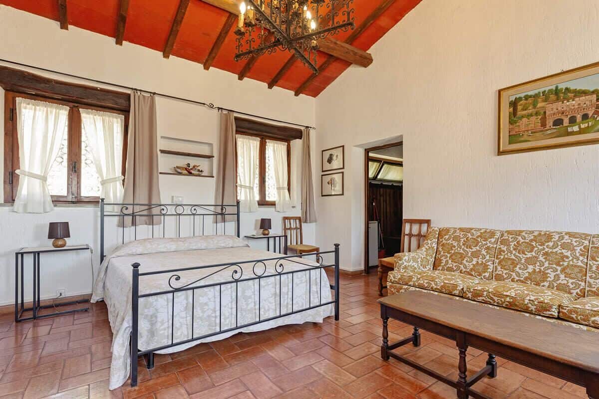 Een slaapkamer met een bed, een houten bankje, een sofa en een kroonluchter.