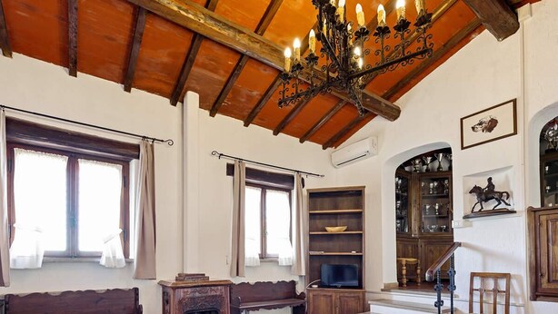 Een klassieke kamer met houten plafond, een kroonluchter, een televisie, een open haard en een trap.