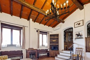 Ein traditionell eingerichteter Raum mit Holzbalkendecke, einer Chandelüster, einem Fernseher, einem Kamin und einer Treppe.