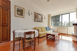 A room with a dining table, wooden chairs, a sofa, and a window with a view. - Agriturismo Tenuta il Solengo (Orbetello)