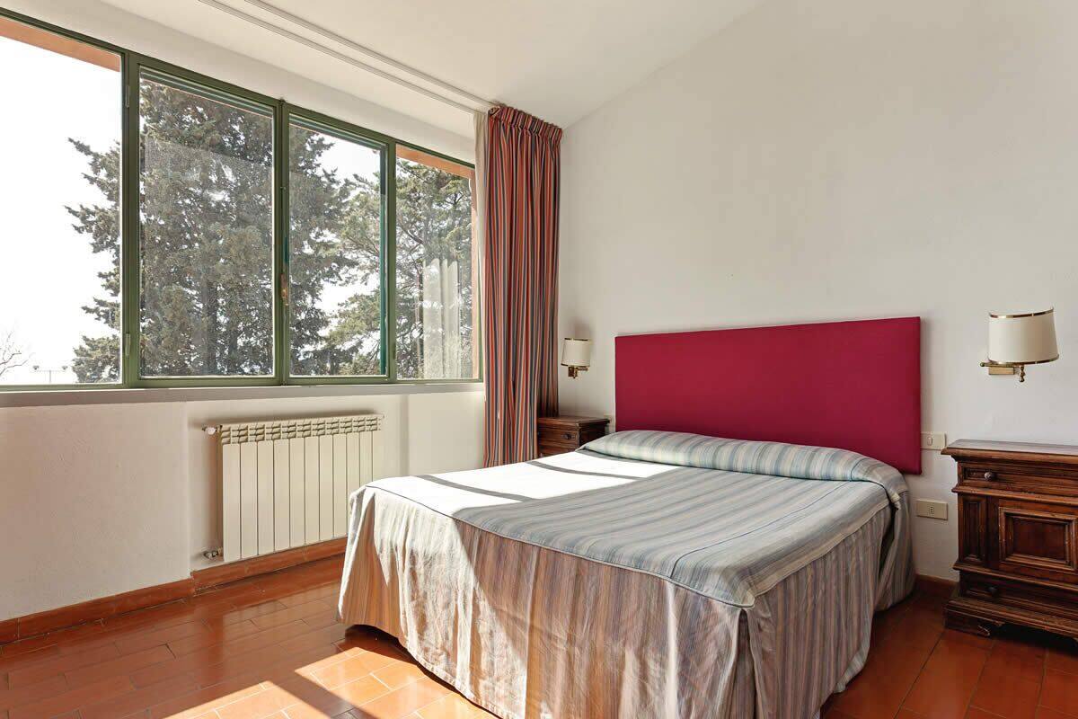 Een slaapkamer met een bed, een raam, een radiator en een nachtkastje.