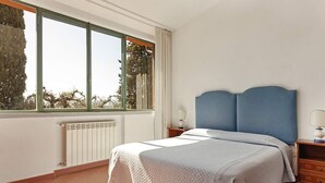 Een slaapkamer met een bed, nachtkastje, raam en radiator.