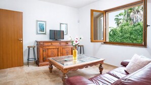 Una sala de estar con un aparador de madera, una mesa de centro de vidrio, un sofá de cuero y un ventanal con vistas a zonas verdes.