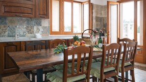 Una mesa de madera para comer con sillas, una cesta de frutas y una botella de vino.