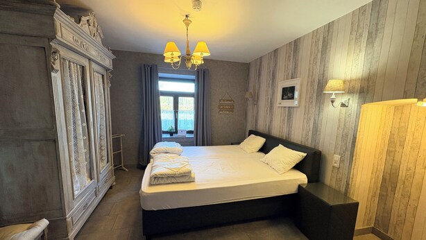 Een slaapkamer met een groot bed, een kledingkast, een bureau en een raam met gordijnen.