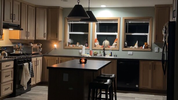 Een moderne keuken met houten kastjes, een centraal eiland, hanglampen en uitzicht door de ramen.