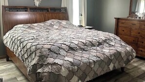 Een slaapkamer met een houten bed, een plafondventilator, een houten dressoir en een wanddecoratie van macramé.