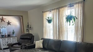 Een woonkamer met een hoekbank, een fauteuil, een bijzettafeltje en een decoratieve spiegel.