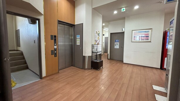 An interior hallway with wooden flooring, a staircase, an elevator, and a vending machine. - Lasting Hotel (Kushiro)