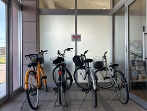 A bicycle rental station with three bicycles, a sign, and a window with a view of the street.