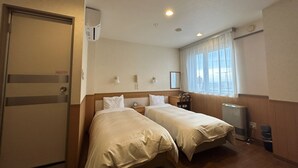 A hotel room with two beds, a desk, a chair, a telephone, and a radiator. - Lasting Hotel (Kushiro)