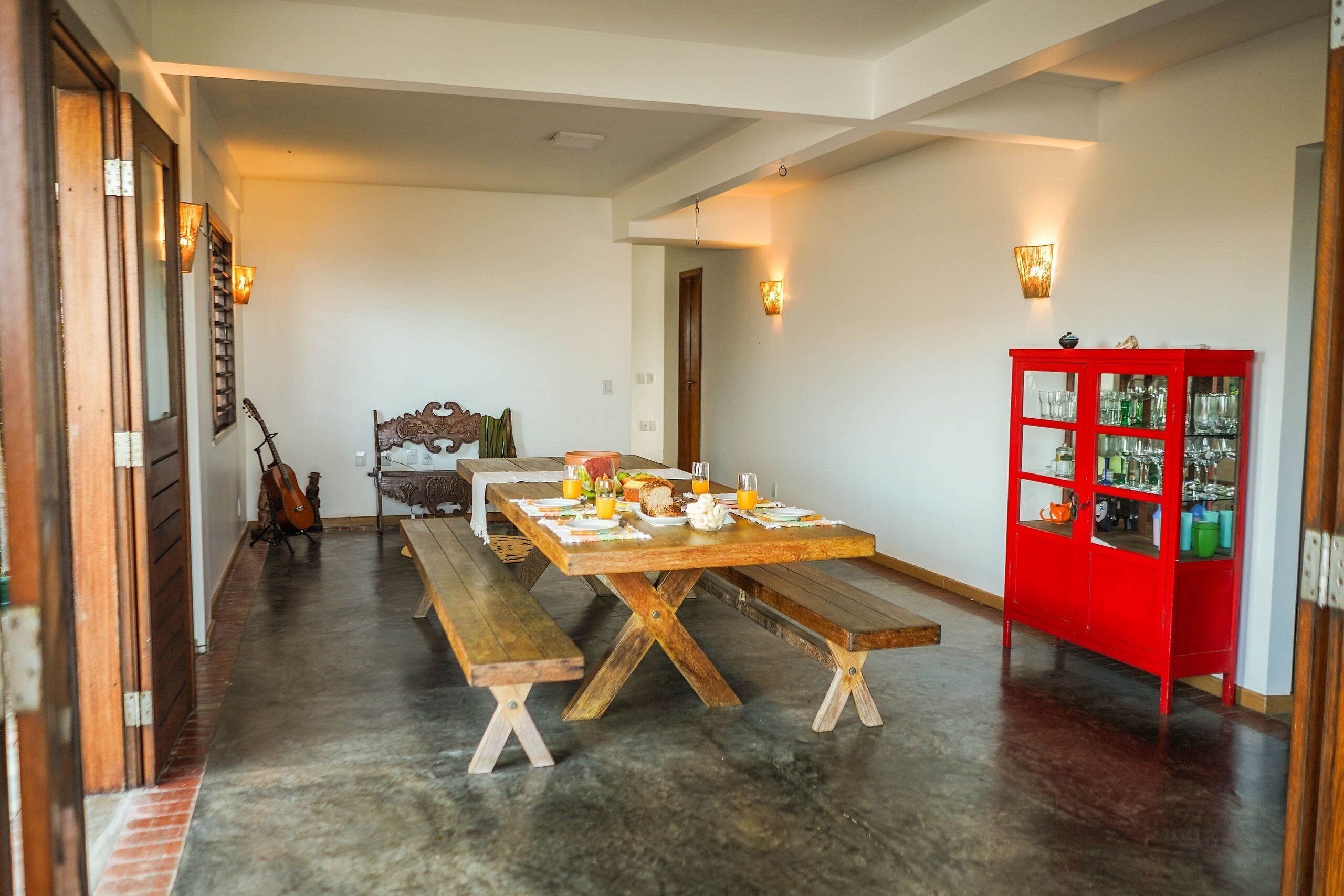A dining area with a long wooden table, benches, and a red cabinet with glass doors.