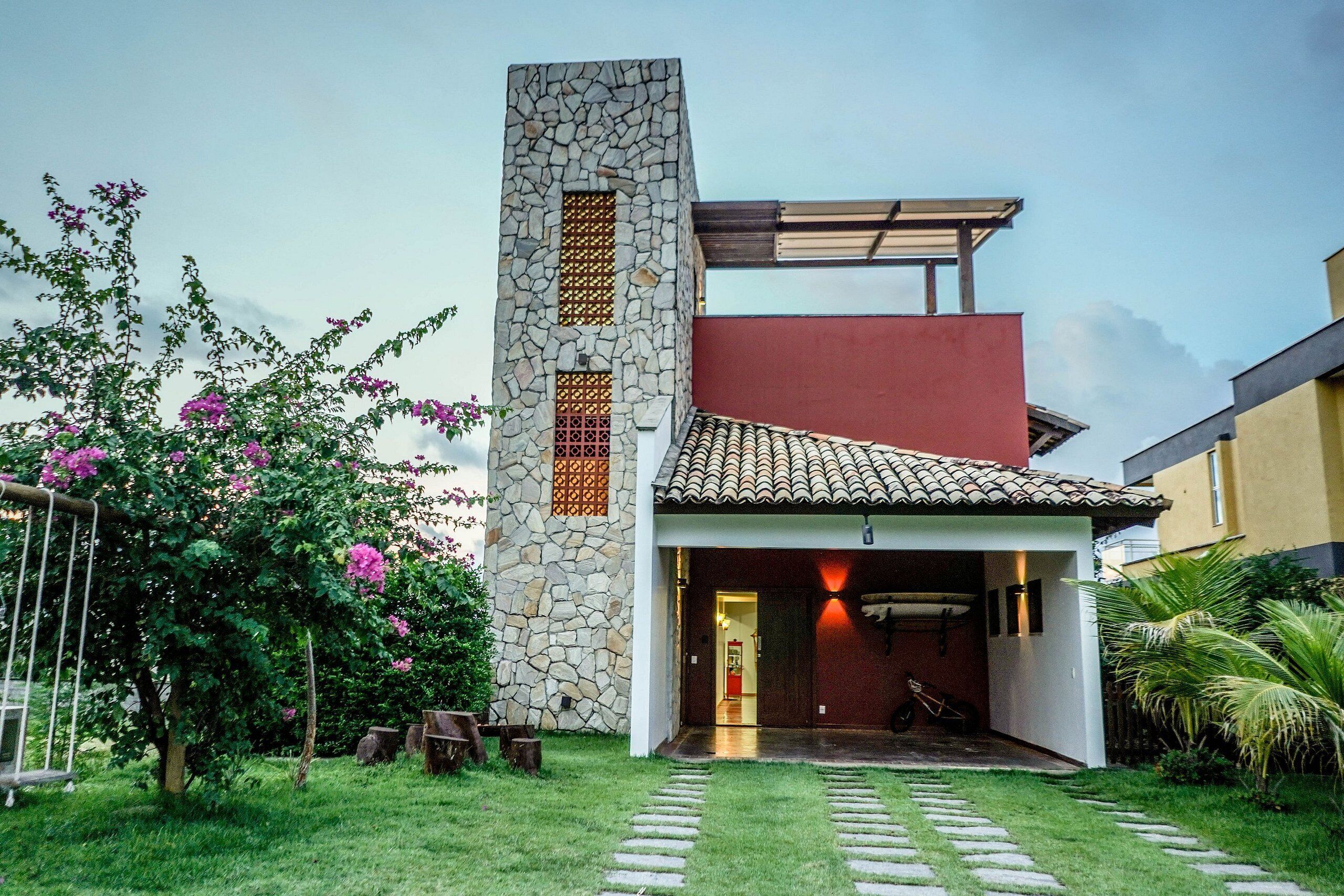 Una casa moderna con una torre de piedra, una sección superior roja y un acceso cubierto.