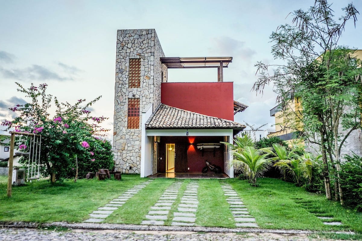 A modern house with a stone facade, a red roof, and a paved driveway leading to a wooden door.