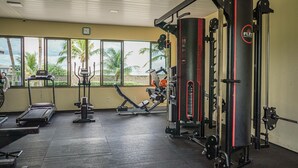 Uma academia com equipamentos de exercício, janelas amplas e vista para palmeiras.
