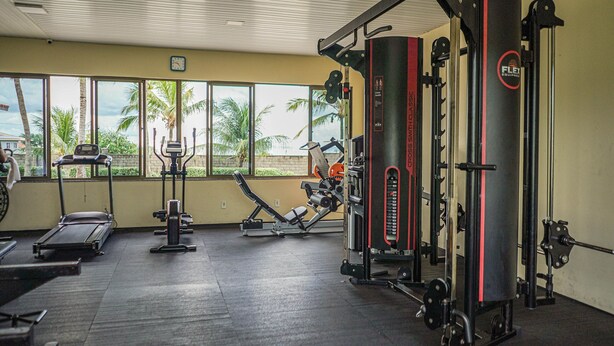 A gym with exercise equipment, large windows, and a view of palm trees. - Summerville #159 - House With Pool by Carpediem (Caucaia)