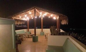 An outdoor patio with a thatched roof, string lights, and seating. - Posada Nomad Hotel (San José del Cabo)