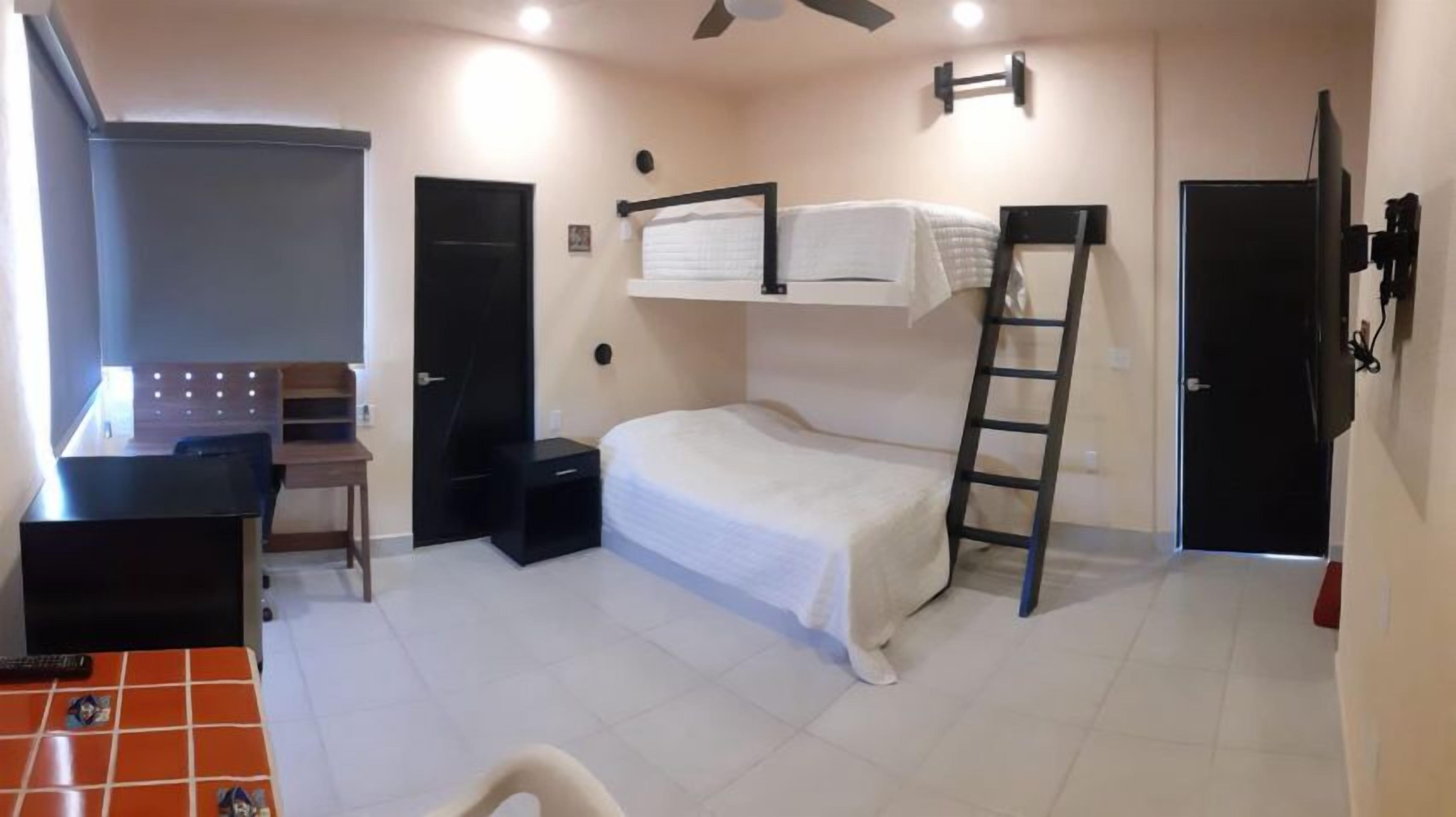 A compact room with a bunk bed, a desk with a chair, a ladder, and a wardrobe.