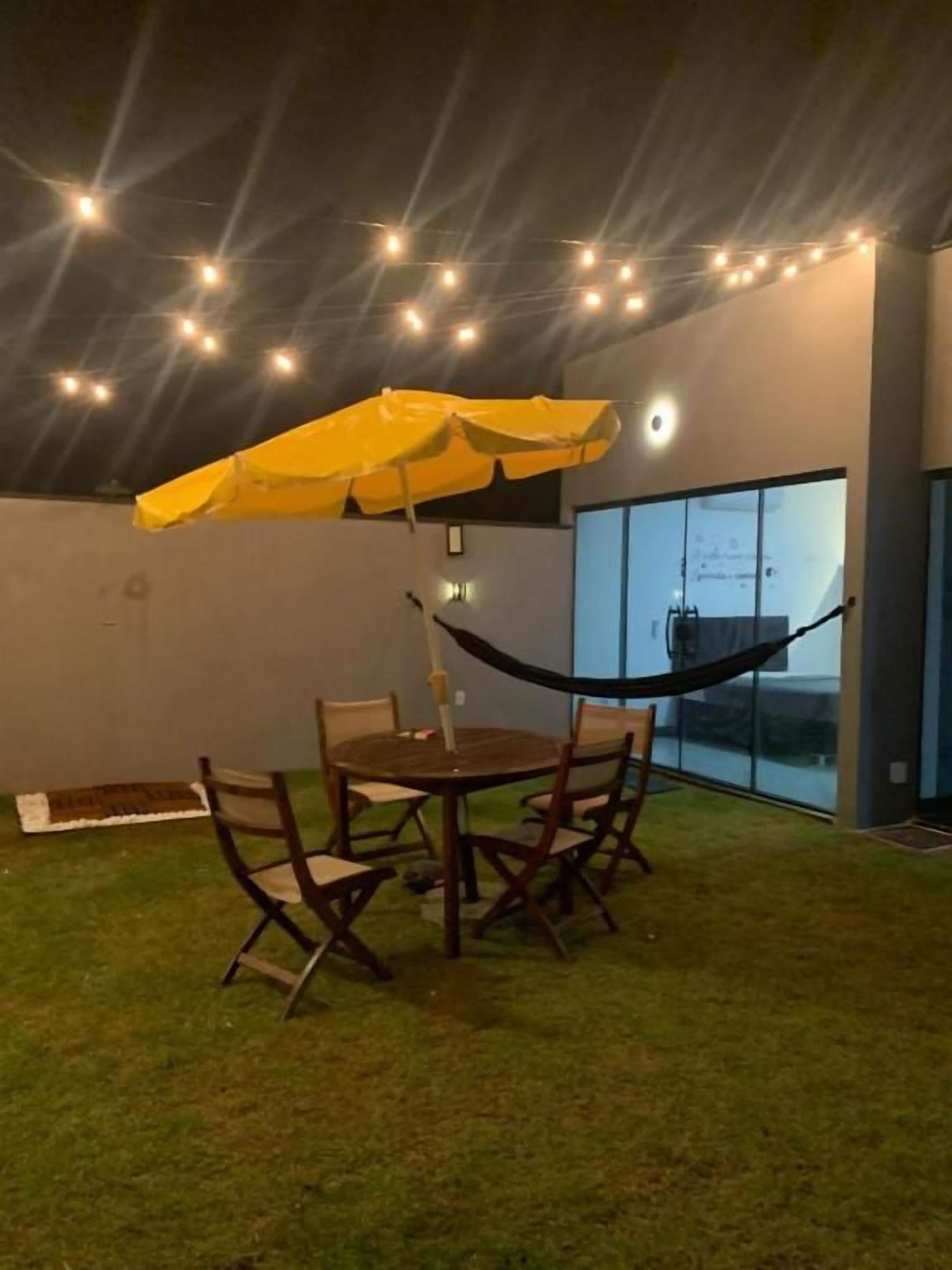 An outdoor seating area with a table and chairs, a yellow umbrella, and string lights.