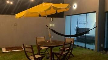 An outdoor seating area with a table and chairs, a yellow umbrella, and string lights.