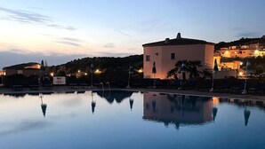 A calm pool reflecting a building and surrounding landscape at dusk. - Sunset Costarossa 1223 - Breathtaking sea view terrace Sardinia (Trinità D'Agultu e Vignola)