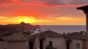 A coastal view with a sunset, rocky terrain, and traditional architecture. - Sunset Costarossa 1223 - Breathtaking sea view terrace Sardinia (Trinità D'Agultu e Vignola)