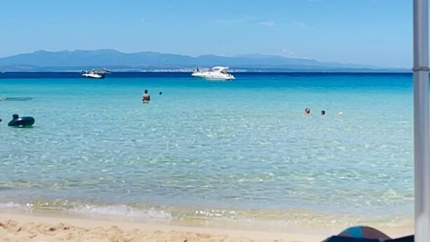 A beach scene with a clear blue sky, calm sea, and a white umbrella. - Sunset Costarossa 1223 - Breathtaking sea view terrace Sardinia (Trinità D'Agultu e Vignola)