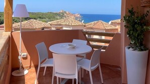 A terrace with a table and chairs, a potted plant, and a view of the sea and buildings. - Sunset Costarossa 1223 - Breathtaking sea view terrace Sardinia (Trinità D'Agultu e Vignola)