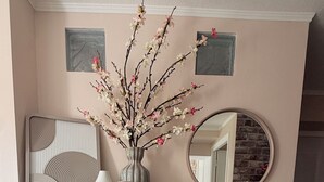Een kamer met een wit kastje, een vaas met bloemen, een spiegel en een wand met een structuur.